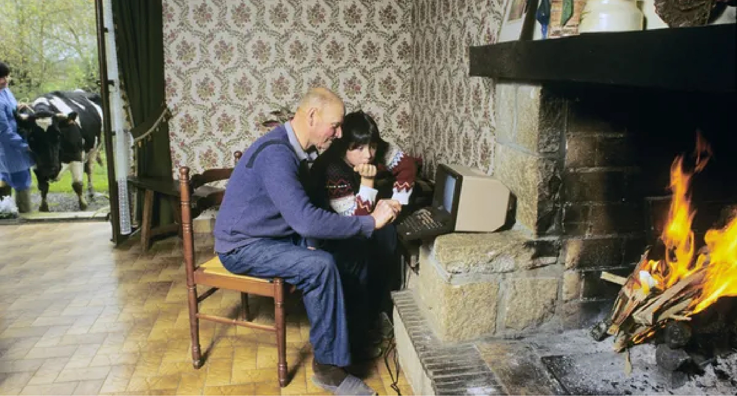 Man and son huddled around a minitel computer in front of a fireplace